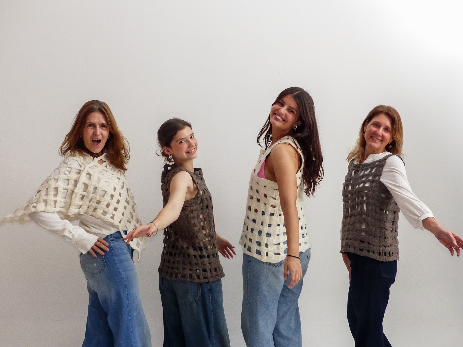 Cuatro mujeres juntas y sonrientes con prendas de nuno fieltro caladas en retícula, en marfil y gris oscuro, con jean.