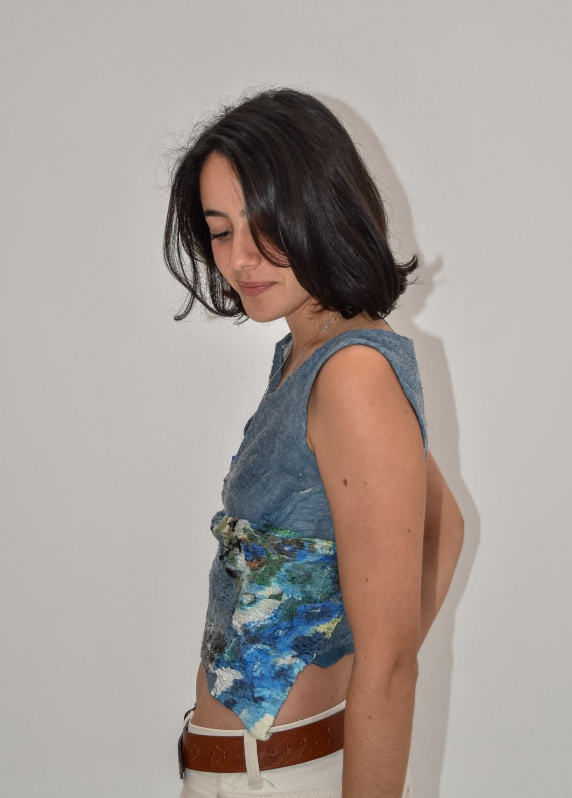 Musculosa corta de nuno fieltro gris azulado con un parche de seda en azules y verdes que termina en punta sobre un pantalón blanco.